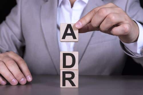 Alternative Dispute Resolution ADR, Adverse Drug Reaction, text written on wooden cubes against the background of a man in a gray suit sitting at a table.