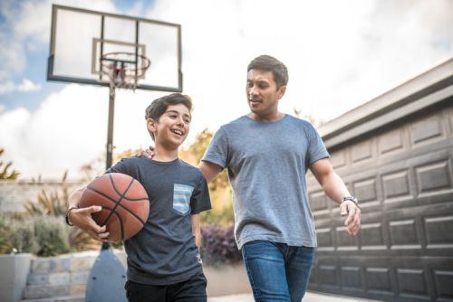 Happy boy after the basketball match with his father. Mid adult man and child are smiling in backyard. They are wearing casuals during weekend concept