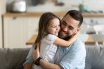 Close up smiling loving young father hugging adorable little daughter, enjoying tender moment, spending weekend together, sitting on cozy couch at home, good family relationship between dad and child concept